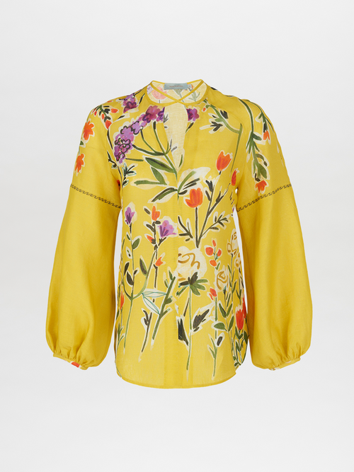 The Molveno Blouse by Silvia Tcherassi features golden yellow linen with a wallflower design in red, purple, and green. It includes high-fashion sleeves, a keyhole neckline, and a loose fit.