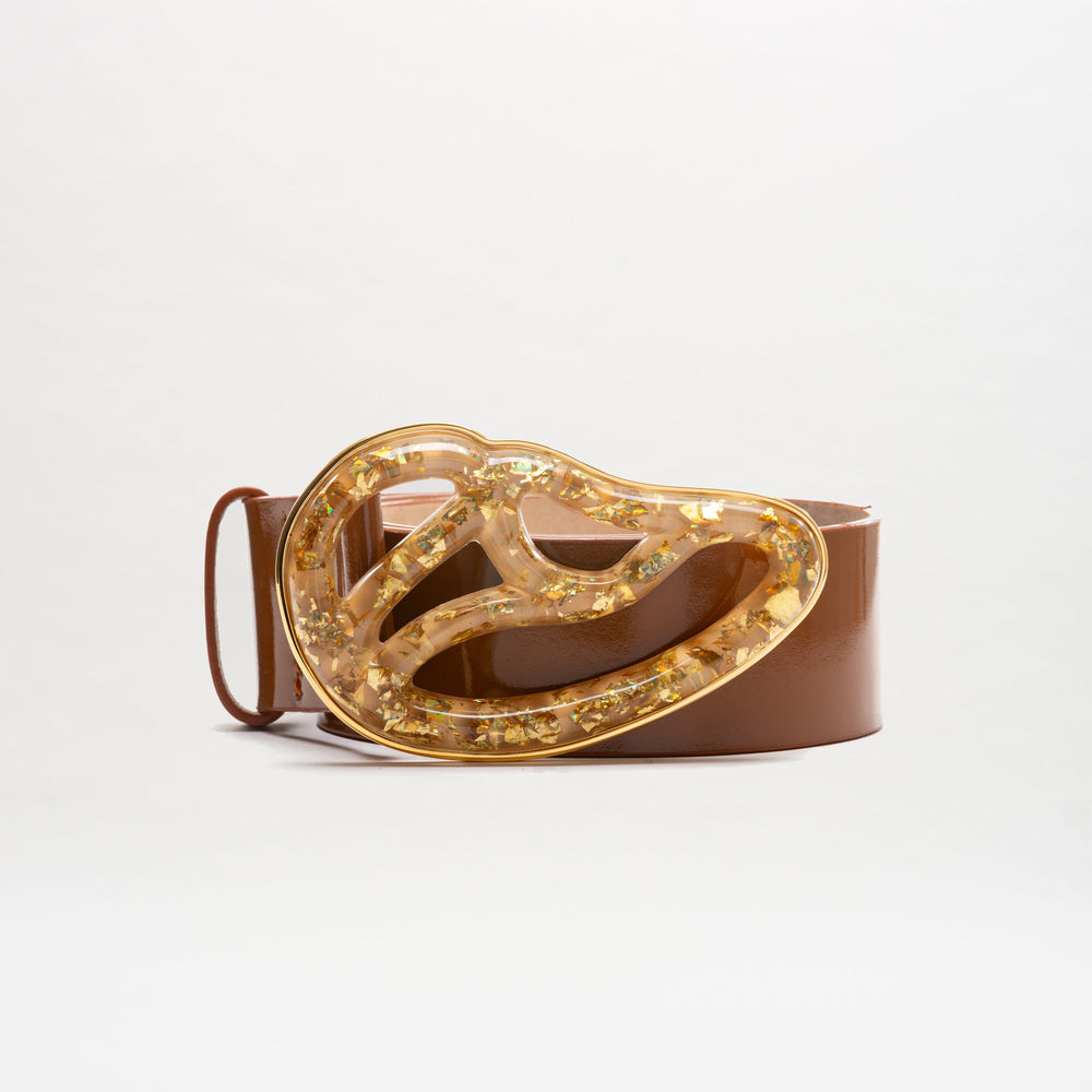The Nala Belt is a wide brown Italian leather belt with a large, abstract Petralux buckle accented by embedded gold flakes. Made in Colombia, it’s displayed against a plain white background.