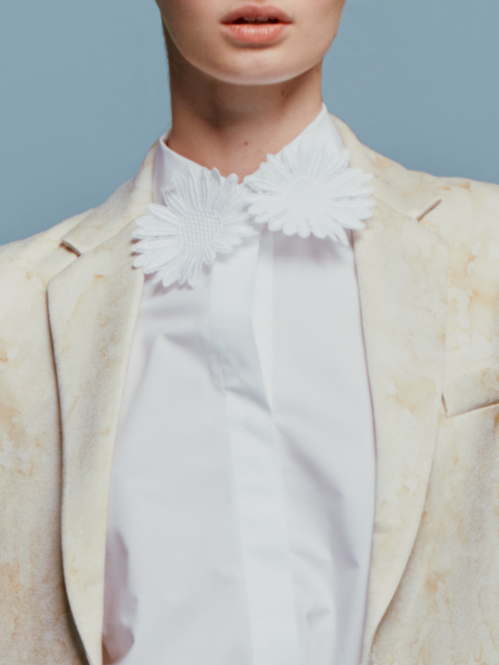 Person dressed in the Naroa Blouse White with a floral shirt and gold belt, standing against a blue background, ready to celebrate September 2nd.