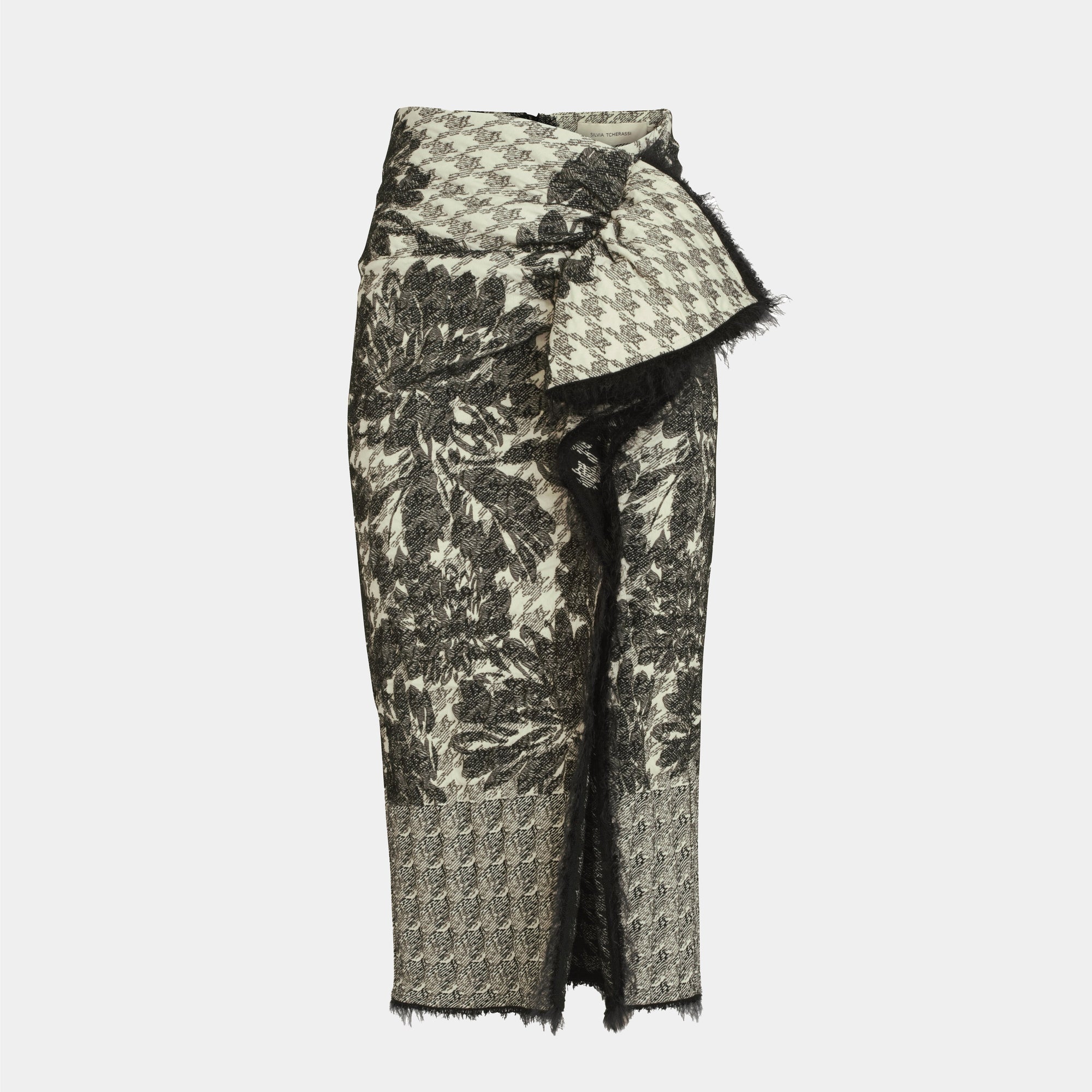 The Nilam Skirt is a high-waisted, knee-length midi with monochrome patchwork, houndstooth and floral patterns, an asymmetrical front fold, draped detail, and raw edges.