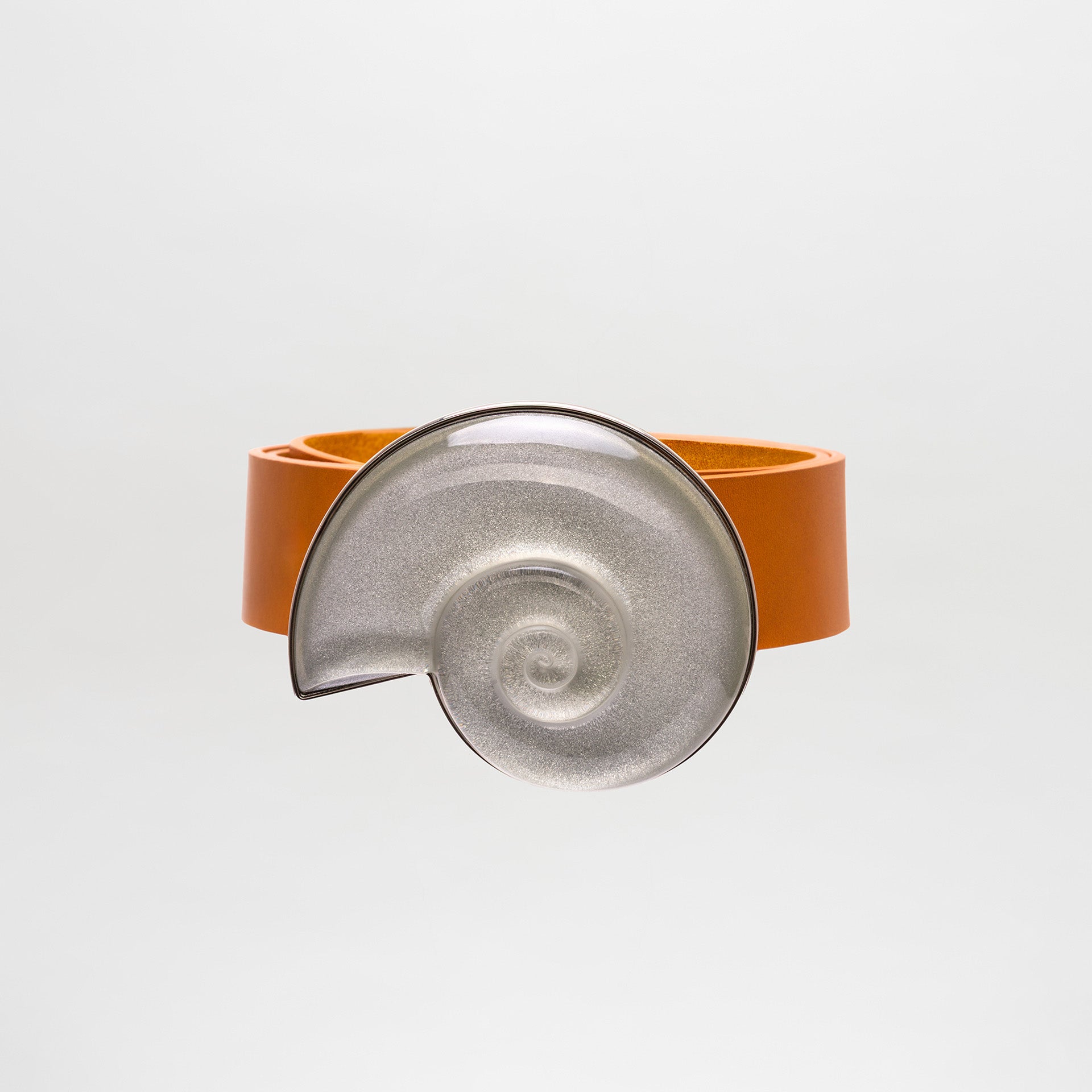 The SVT DESIGNS Nautilus Belt is a wide orange 100% leather accessory featuring a large, metallic, spiral-shaped centerpiece reminiscent of a snail shell, shown on a light gray background.