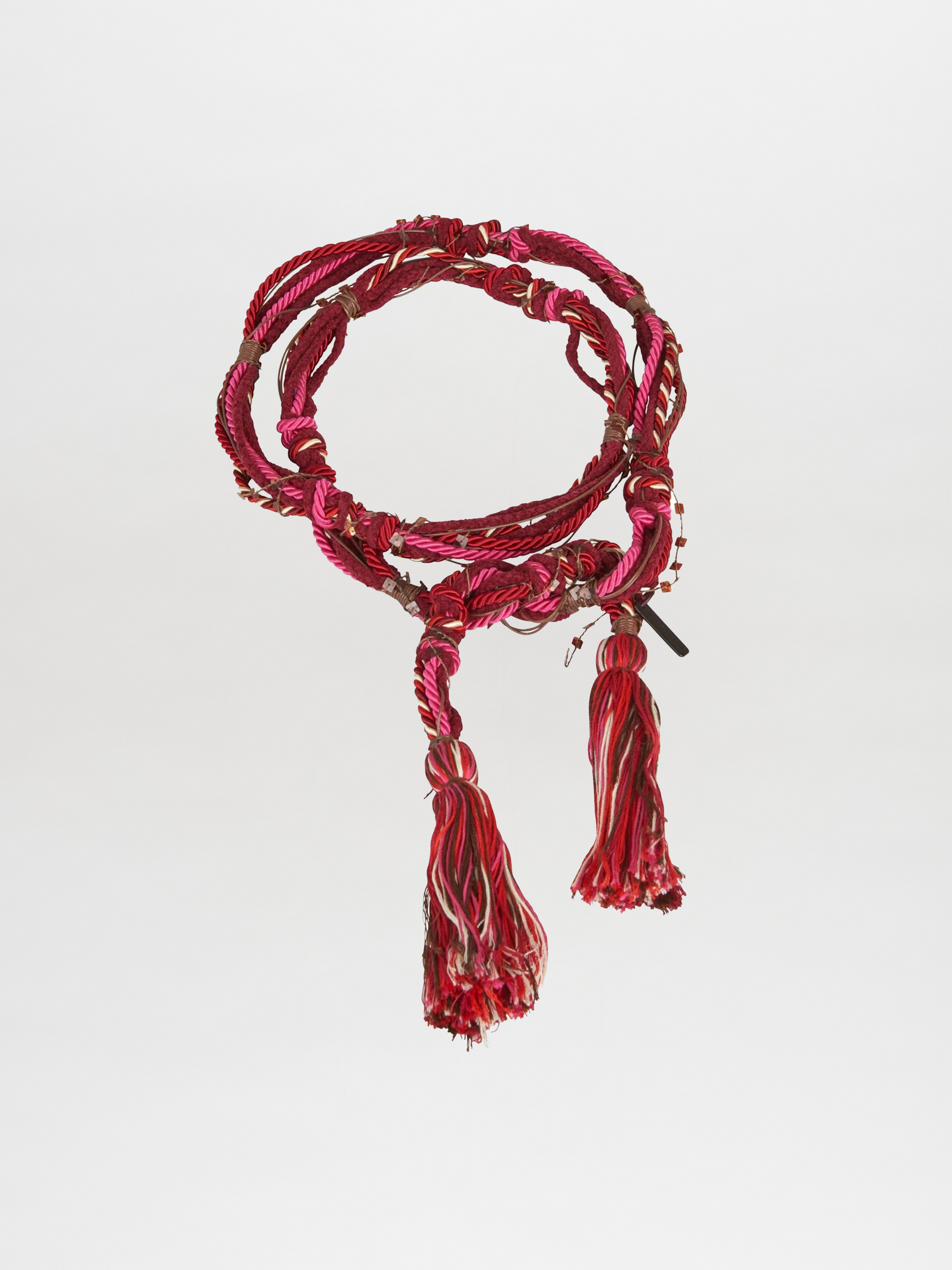 The Nellie Belt Fucshia by Silvia Tcherassi features coiled red, pink, and white threads with two large tassels—an eye-catching accessory from Pre Fall 2023, shown on a plain white background.