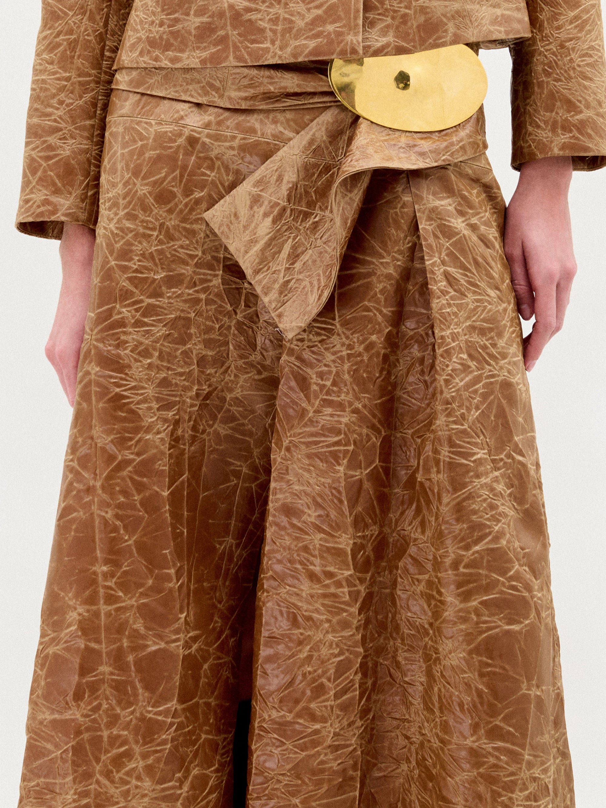 A person stands against a plain background wearing the Olga Skirt in color Caramel.