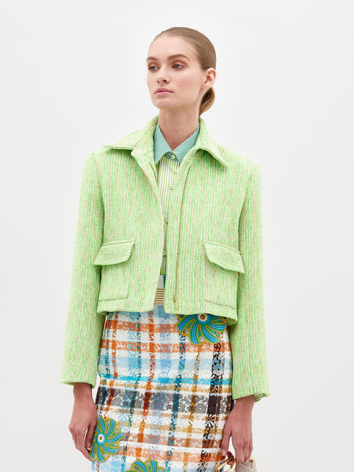 Person wearing the Perla Jacket Lime over a striped shirt and a colorful patterned skirt against a plain white background, showcasing a pre-order fashion piece for 2025.