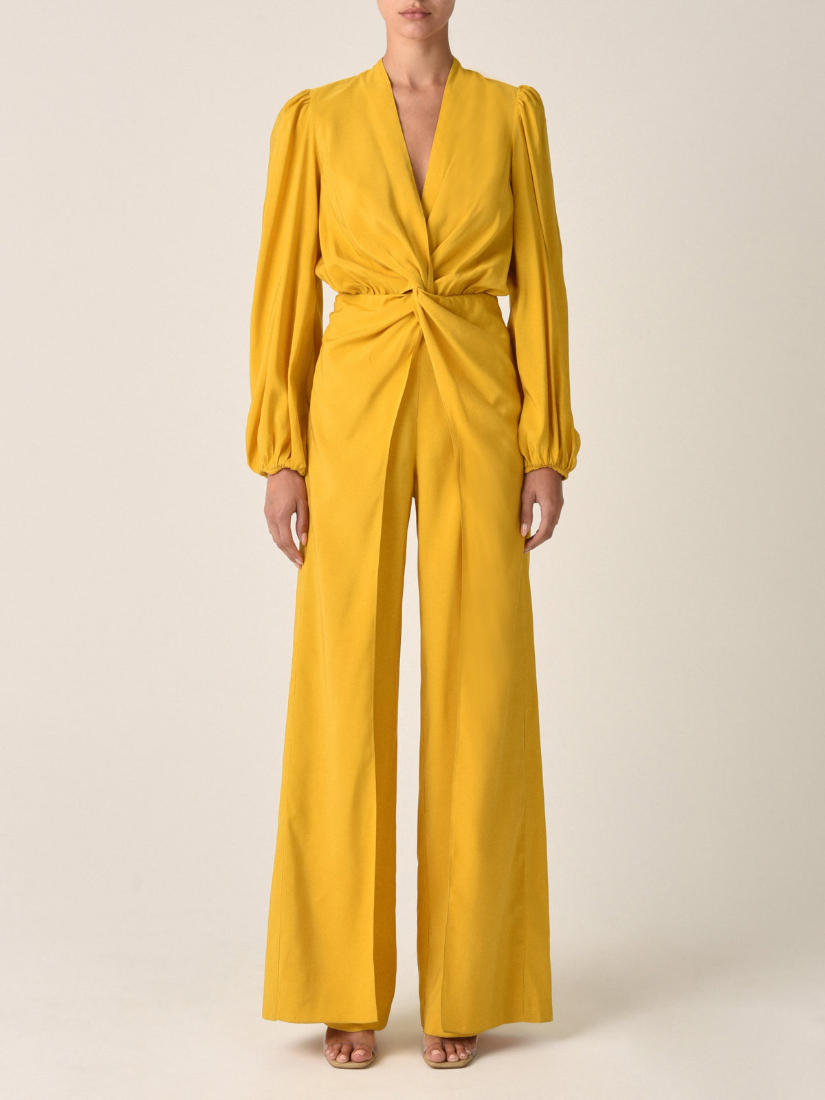 The Arnetia Jumpsuit Amber in mustard yellow features long puffed sleeves, a keyhole neckline, and a twisted knot detail at the front, capturing the versatile elegant appeal of the Silvia Tcherassi aesthetic.