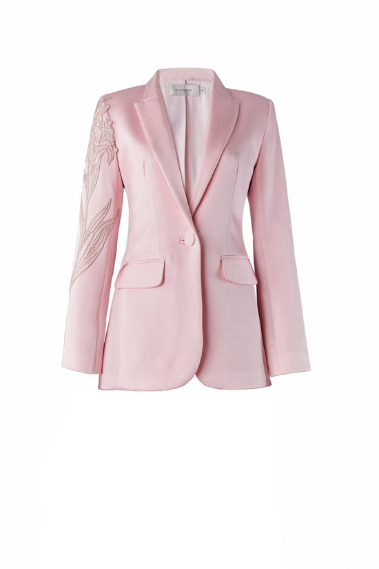 Profile view of a person with long hair tied back, wearing the Rebeca Jacket Pink, a light pink blazer adorned with intricate embroidery on the shoulder; pre-order now for delivery by February 1st, 2025.