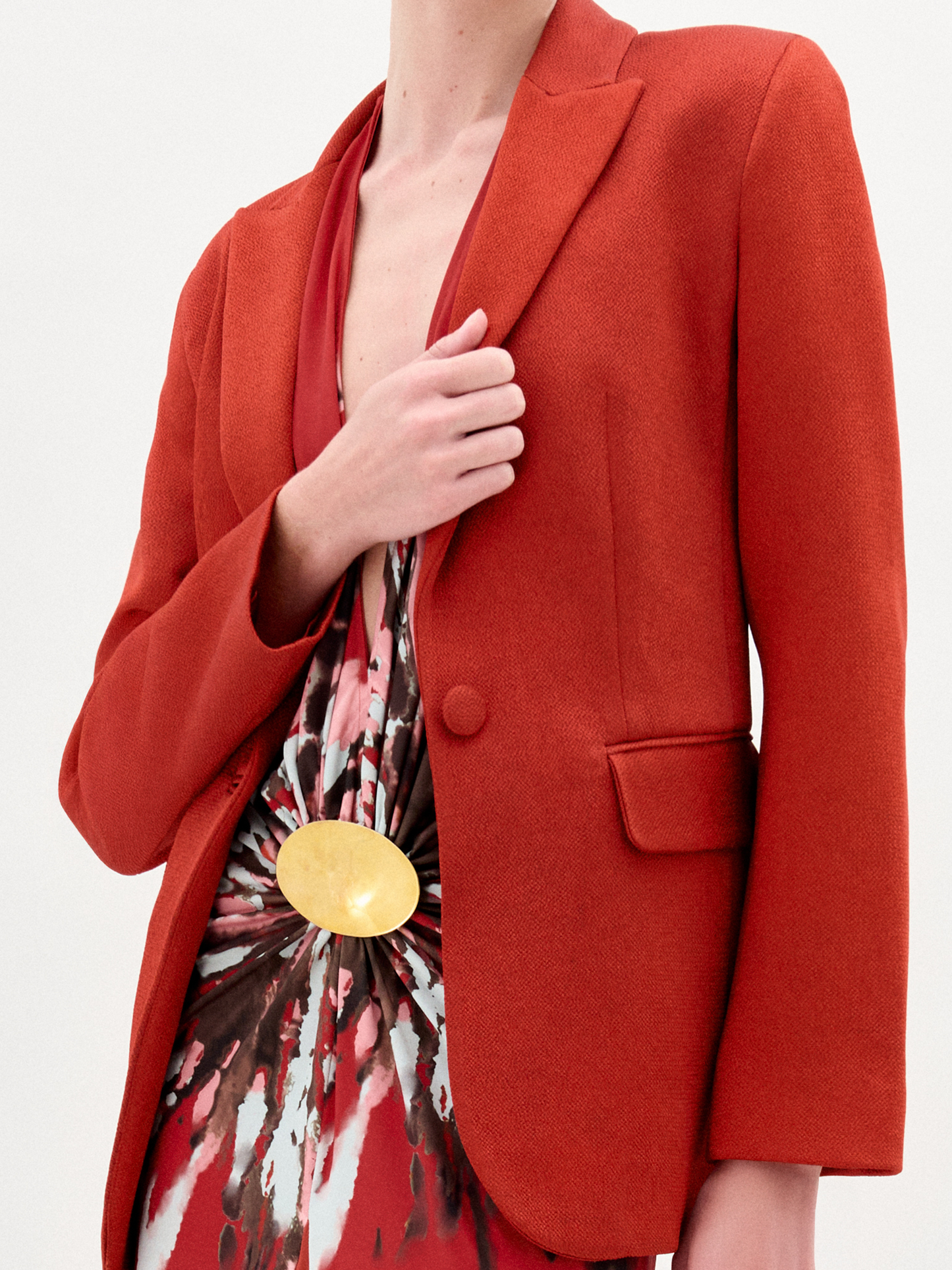 A person wearing the Rebeca Jacket, a fitted red blazer made from Italian fabric, layered over a patterned red and beige dress, stands against a plain light background.