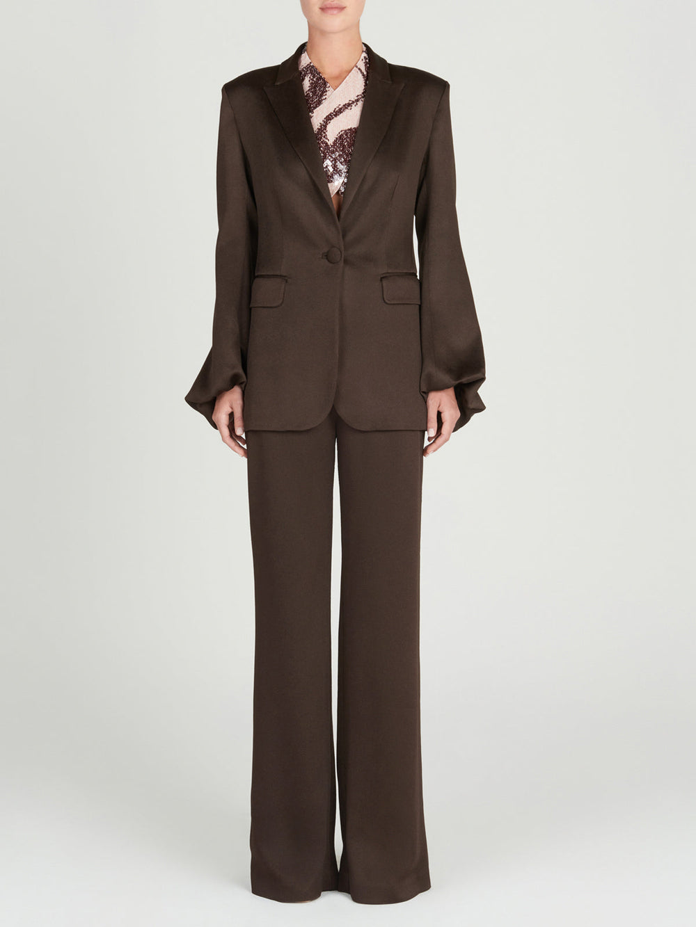 A person faces forward wearing a dark brown Silvia Tcherassi Coco Blazer with wide-leg trousers and a hammered satin statement blouse, set against a plain light background.