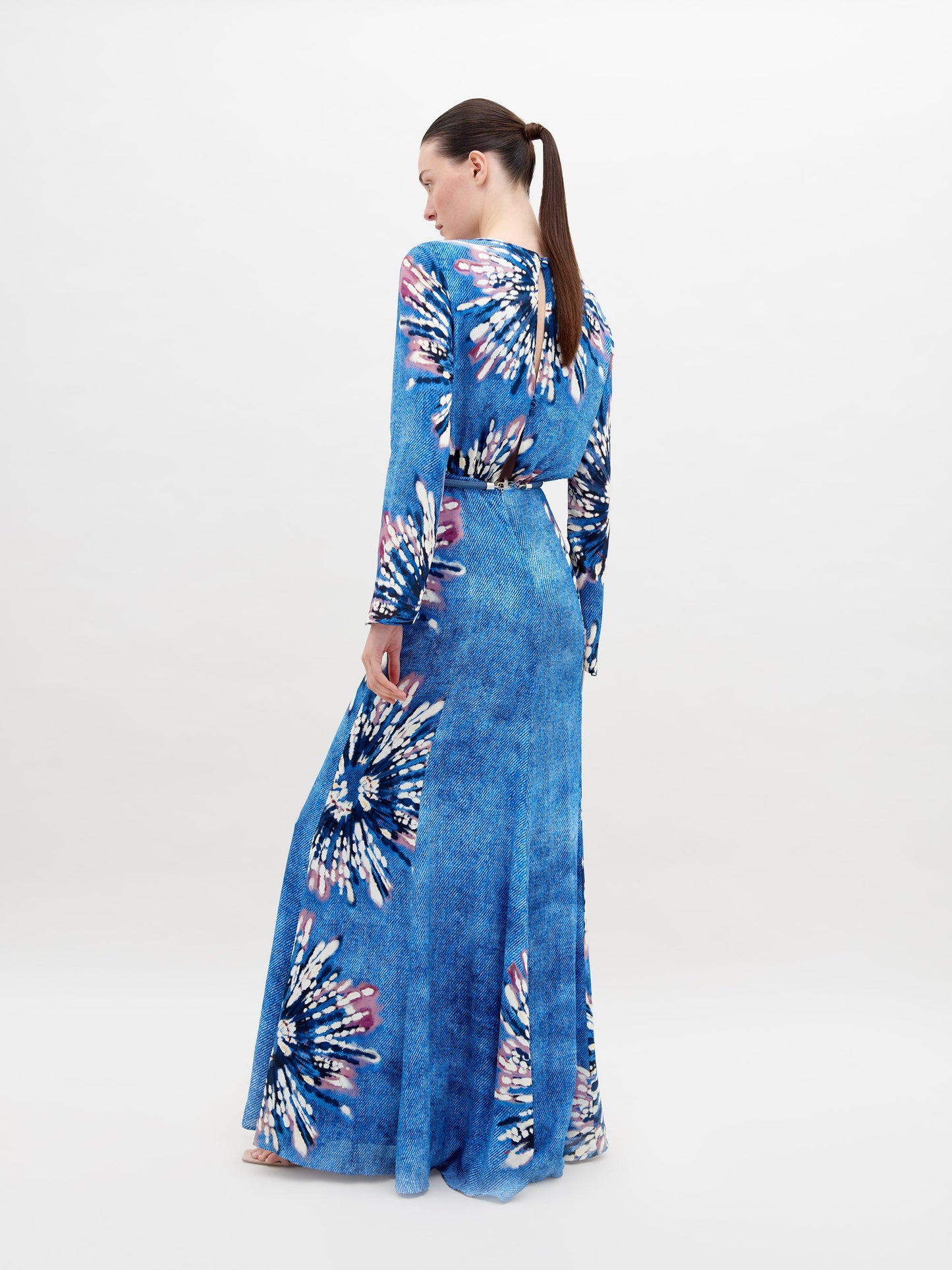 A person stands wearing the Ravenna Dress Aciano Flower, looking off to the side against a plain white background. Pre-order now to ensure it arrives by November 15th, 2024.