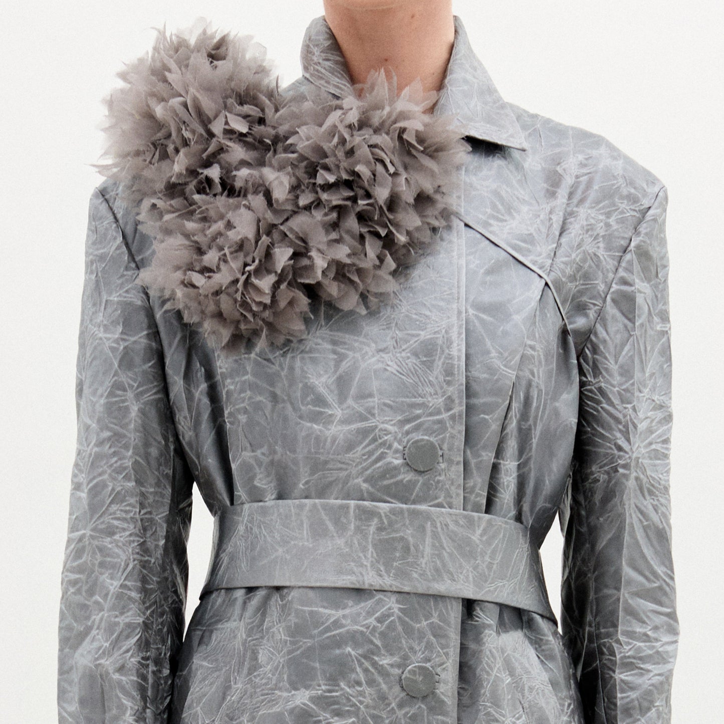 A person wears a light grey, textured coat made from Italian fabric, styled with the Romy Collar Piece—a large, ruffled, fluffy grey accessory attached near the left shoulder.