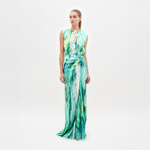 A person stands against a plain white background wearing the Samaira Dress by SVT DESIGNS. This elegant maxi dress features a green, white, and yellow abstract print inspired by Italian textiles, with a sleeveless design, ruched waist for sophistication, and neatly pulled-back long hair.