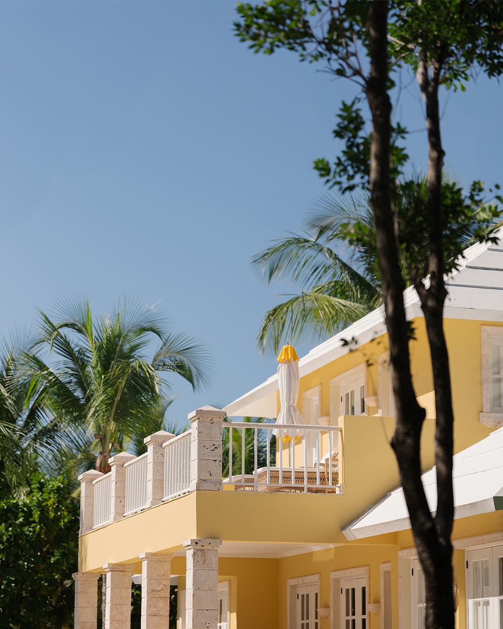 Yellow building with a balcony and palm trees under a clear blue sky