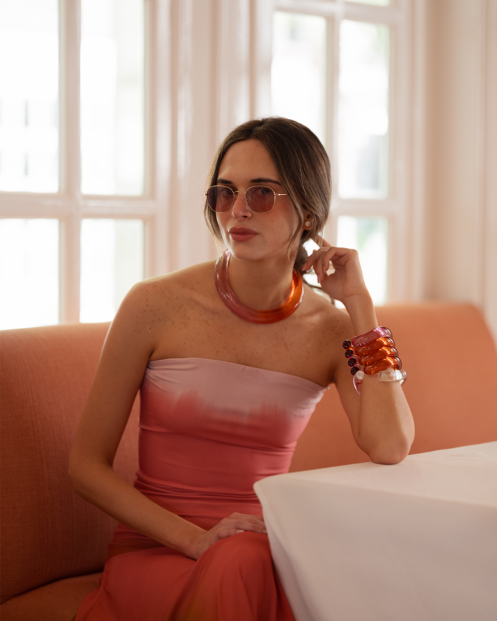 Woman in a strapless pink dress with orange accents sitting on a couch.