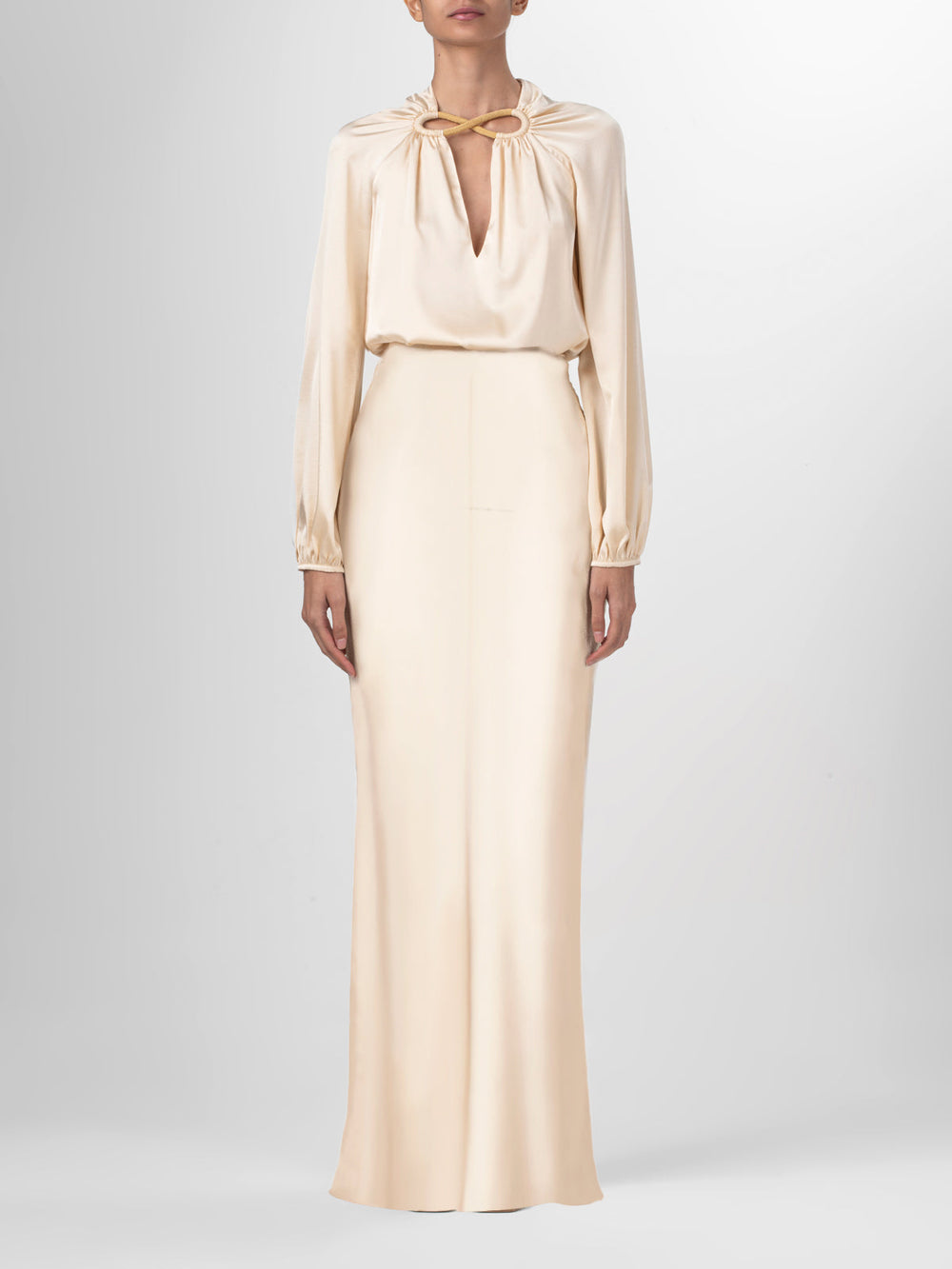 A person wears the Laurina Skirt, a high-waisted, cream-colored maxi skirt with long sleeves and a high neckline featuring a keyhole cutout and tied bow. Made in Colombia, it stands out against a plain light background.