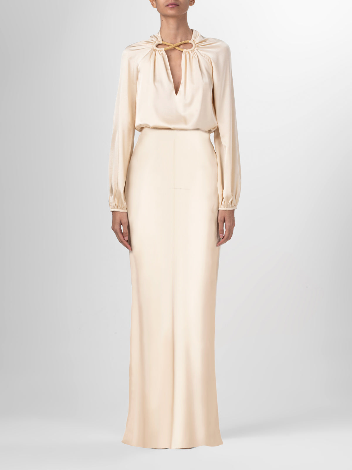 A person wears the Laurina Skirt, a high-waisted, cream-colored maxi skirt with long sleeves and a high neckline featuring a keyhole cutout and tied bow. Made in Colombia, it stands out against a plain light background.