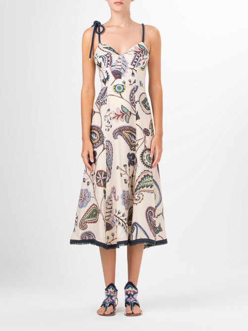 A person stands facing forward in a sleeveless, ankle-length Dalil Dress by Silvia Tcherassi US, featuring a vibrant paisley and floral design. Their hands rest at their sides, complemented by matching sandals against a plain white background that highlights the ensemble.