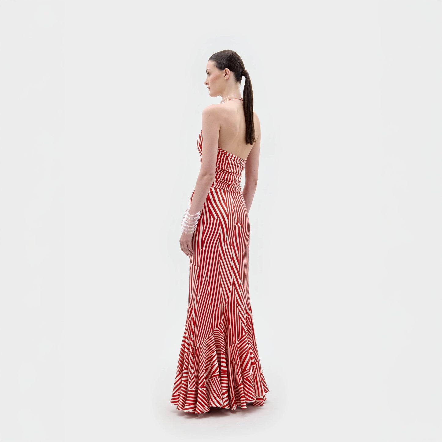 A woman with a ponytail and white bracelets on her left wrist faces away at an angle, modeling the Florina Skirt by SVT DESIGNS. The red and white striped mermaid silhouette skirt is set against a plain white background.