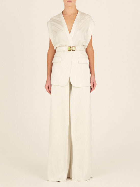 A person wearing the Silvia Tcherassi Keith Vest Moonstone, a cream-colored sleeveless V-neck top with a waist-cinching belt and wide-legged pants, featuring an abstract motif in a monochromatic palette with a structured yet relaxed fit.