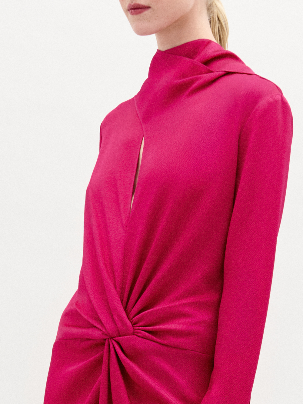 A woman poses in the Sue Dress, a vibrant pink, long-sleeved maxi made from luxurious Italian fabric with a gathered knot at the waist, set against a plain white background.