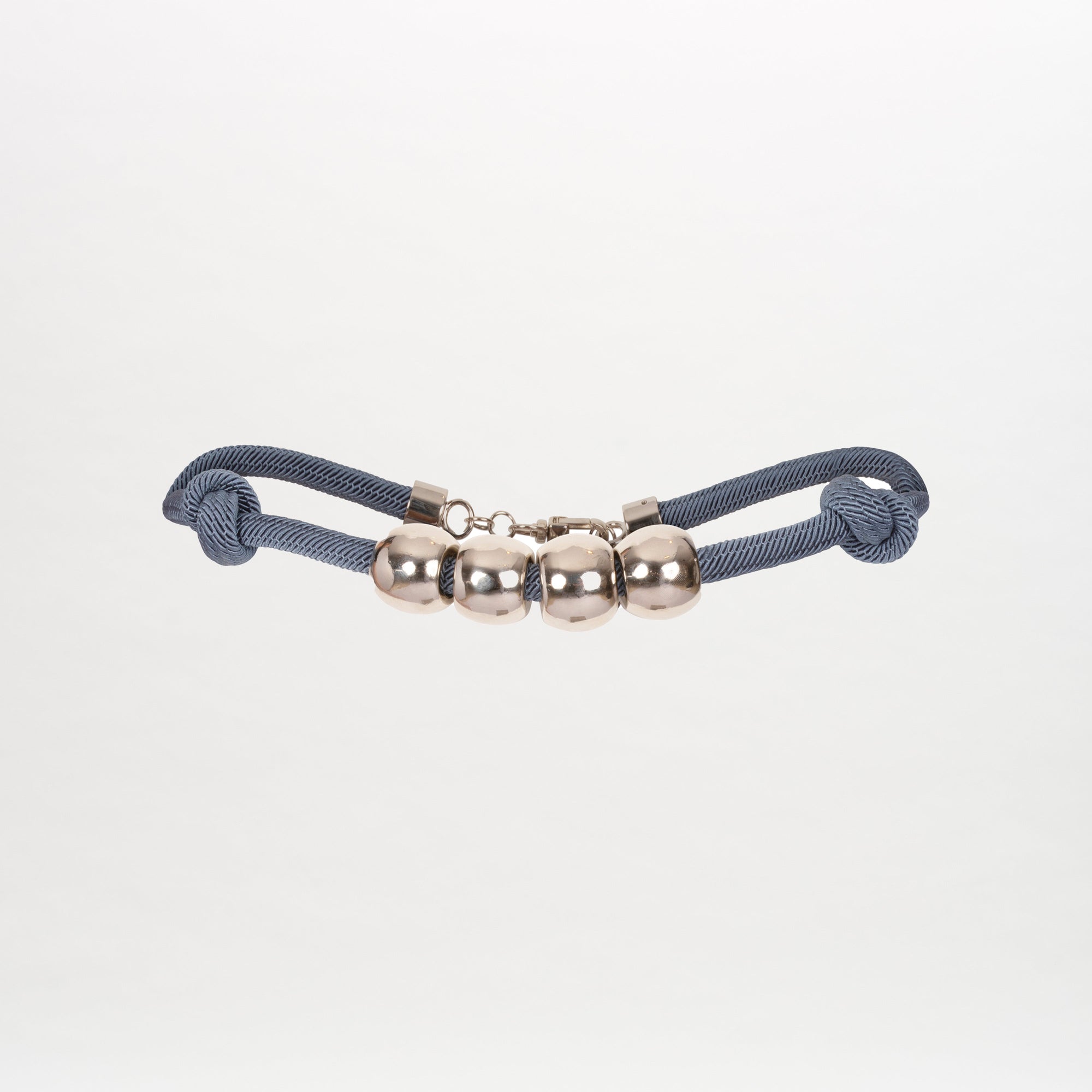 The Sam Belt by SVT DESIGNS features a blue braided cord with four metallic sphere beads at its center. The ends are elegantly knotted, and silver-tone embellishments shine against a plain white background.