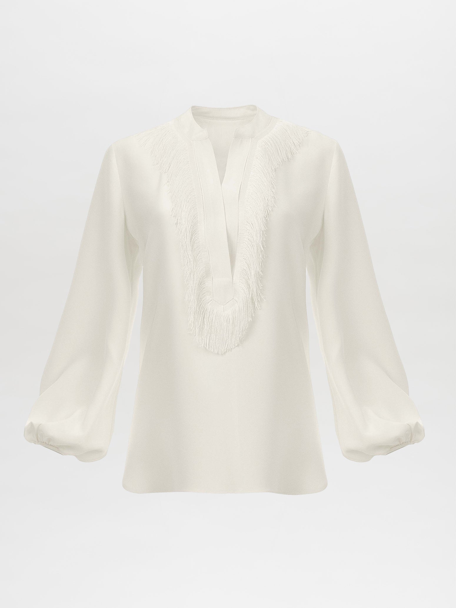 The Sanford Blouse White by SilviaTcherassiEU embodies effortless elegance with its luxurious silk fabric, long billowy sleeves, and a V-neckline with fringe detailing, showcased against a plain white background.