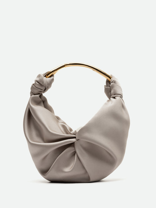 The Sofia Bag Small by SVT DESIGNS is a beige, crescent-shaped handbag with a gold-toned handle. Crafted from luxurious Italian textile, it features artfully knotted ends for a draped effect. Its minimalist design exudes elegance against a plain white background.