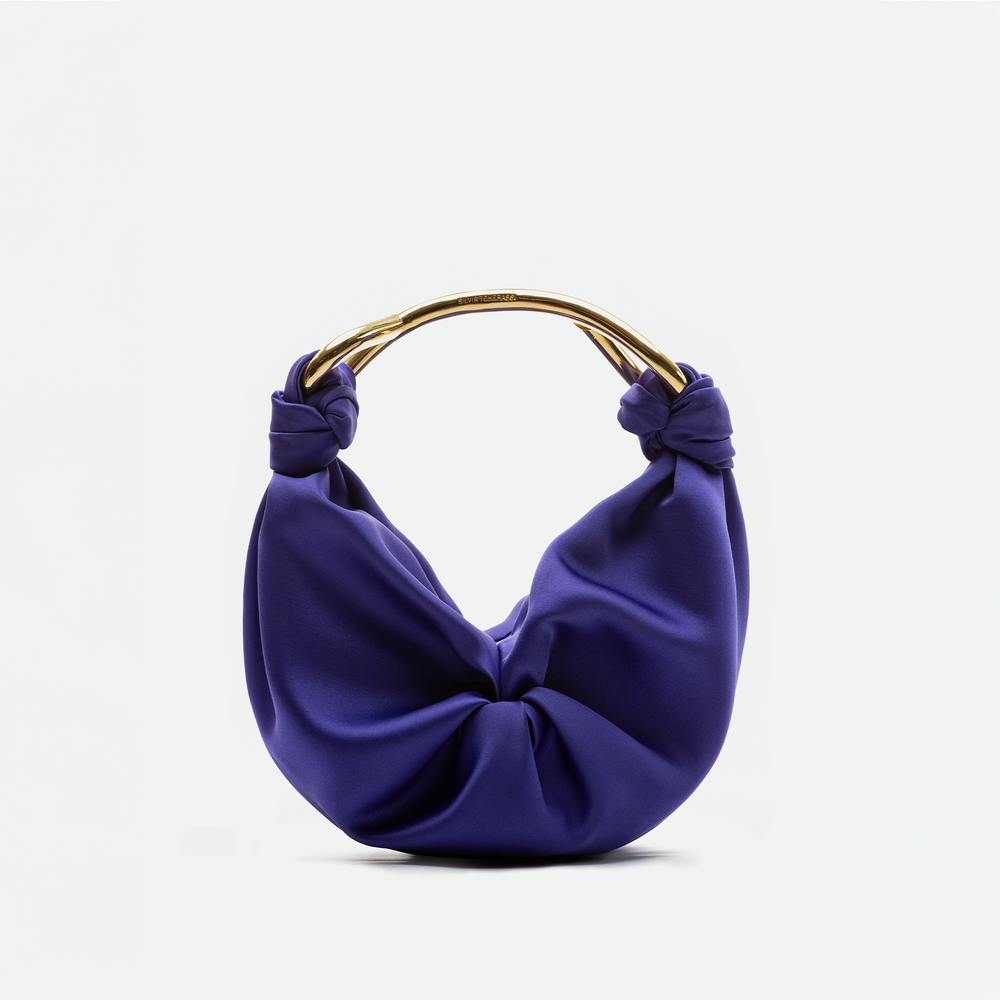 The Sofia Bag Small by SVT DESIGNS is a purple bag with gathered Italian fabric, gold-toned handle, and knot details on each side, shown against a plain white background.