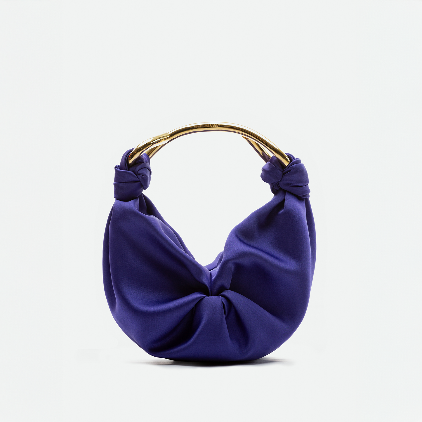 The Sofia Bag Small by SVT DESIGNS is a purple bag with gathered Italian fabric, gold-toned handle, and knot details on each side, shown against a plain white background.