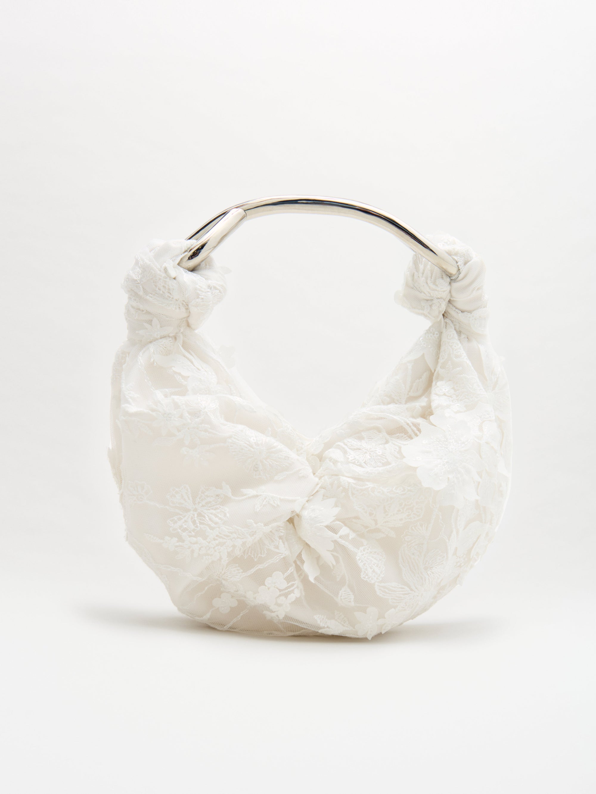 The Sofia Bag Small by SVT DESIGNS is a white handbag with a rounded silver handle, soft ruched design, and delicate floral lace overlay, shown against a plain white background.