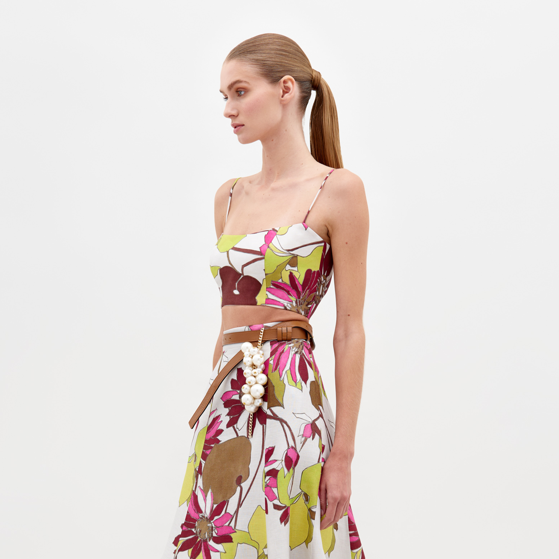 A woman stands against a white background wearing the SVT DESIGNS Trini Top with thin straps and a fitted silhouette. She has a neutral expression and her hair is pulled back in a ponytail.