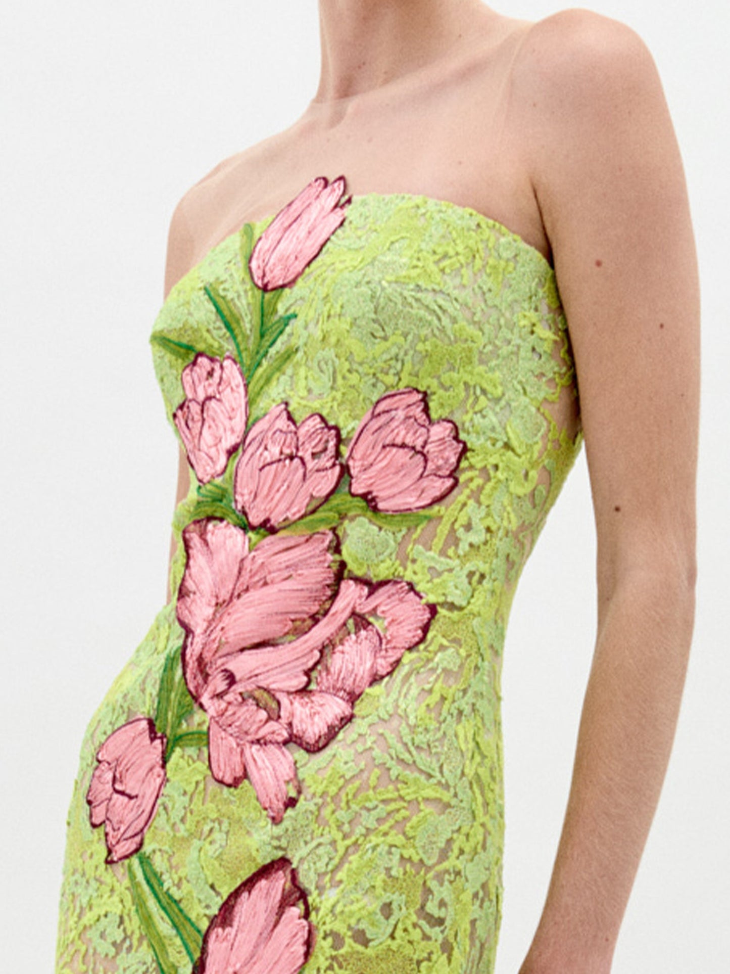 A person wears the Tulip Dress—a strapless style made from sheer green lace with large pink floral embroidery—shown from shoulders to mid-thigh against a plain white background.