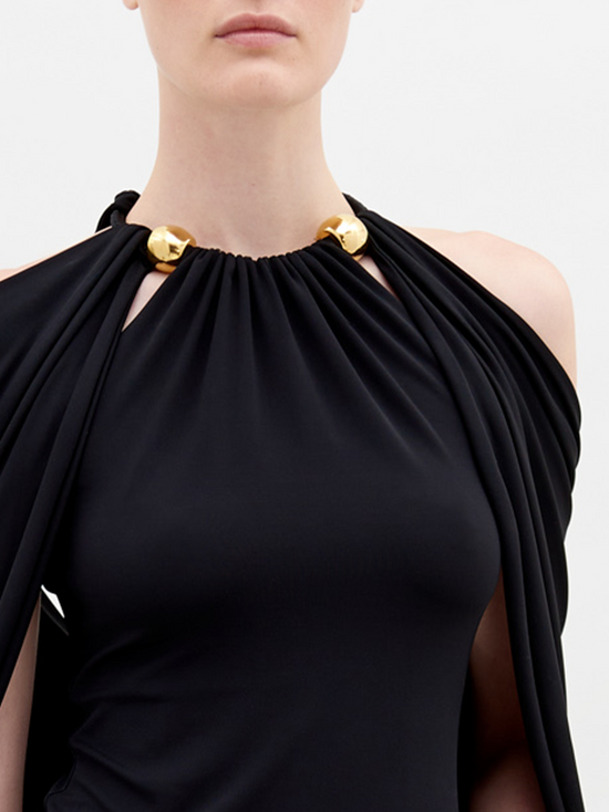 A person with tied-back hair wears a Tabatha Blouse Black with gold accents and a matching gold bracelet, standing against a plain white background. This stylish ensemble is available for pre-order now, with a ship by date of November 15th, 2024.