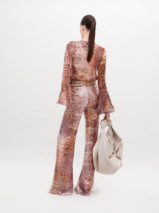 Person wearing a long-sleeved, patterned top and matching Avellino Pant Peach Animal Print with a cinched waist, holding a large beige bag in a white studio setting. Pre-order now to ensure delivery by the ship by date of November 15th, 2024.