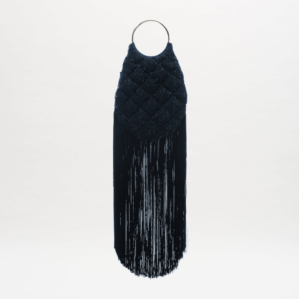 The Toblach Bag by SVT DESIGNS is a dark, oval-shaped Jacquard bag with a quilted texture, metallic top handles, and long black fringe at the bottom, shown against a plain white background.