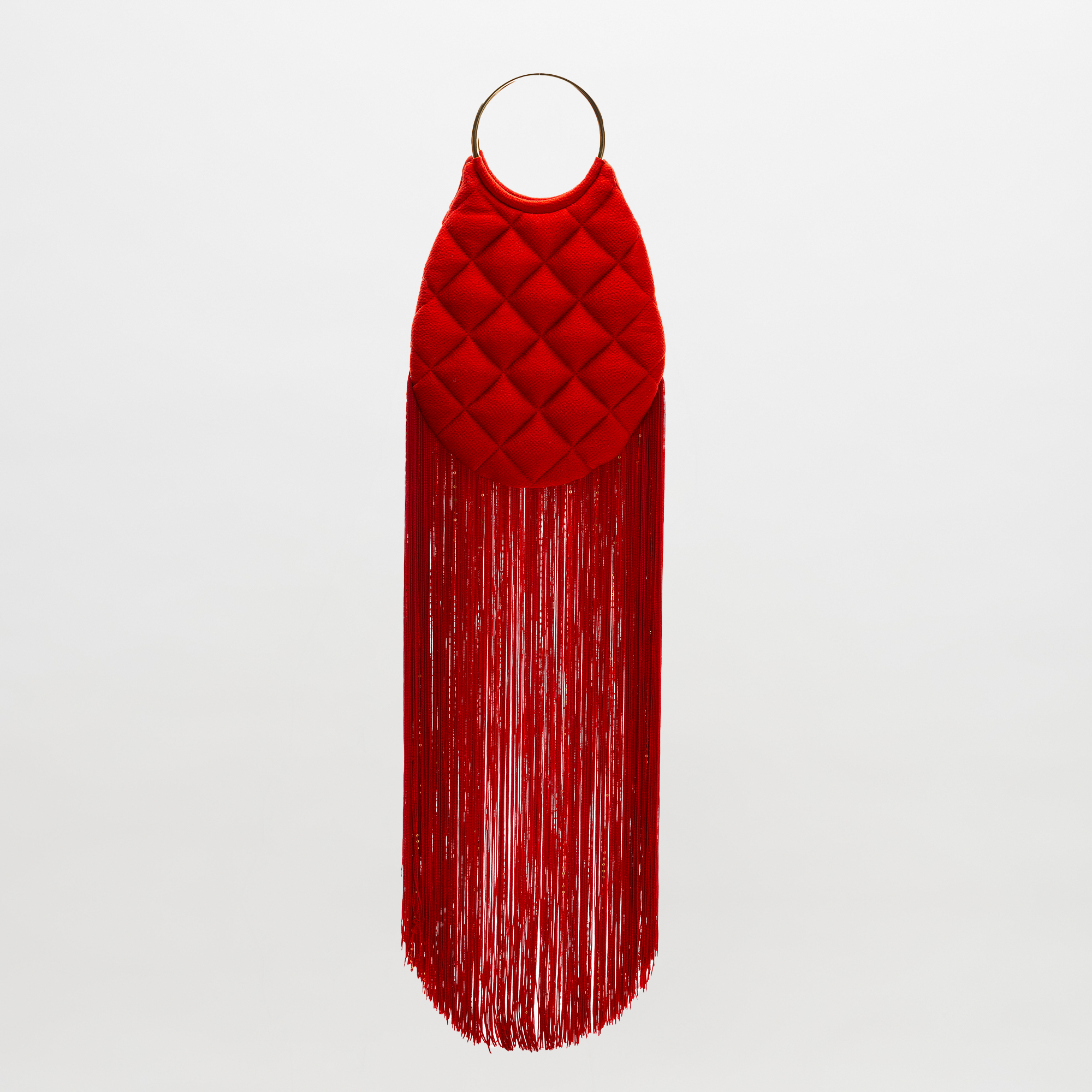 The SVT DESIGNS Toblach Bag is a red handbag with a quilted oval top, metallic top handles, and long fringe at the bottom, shown against a plain white background.