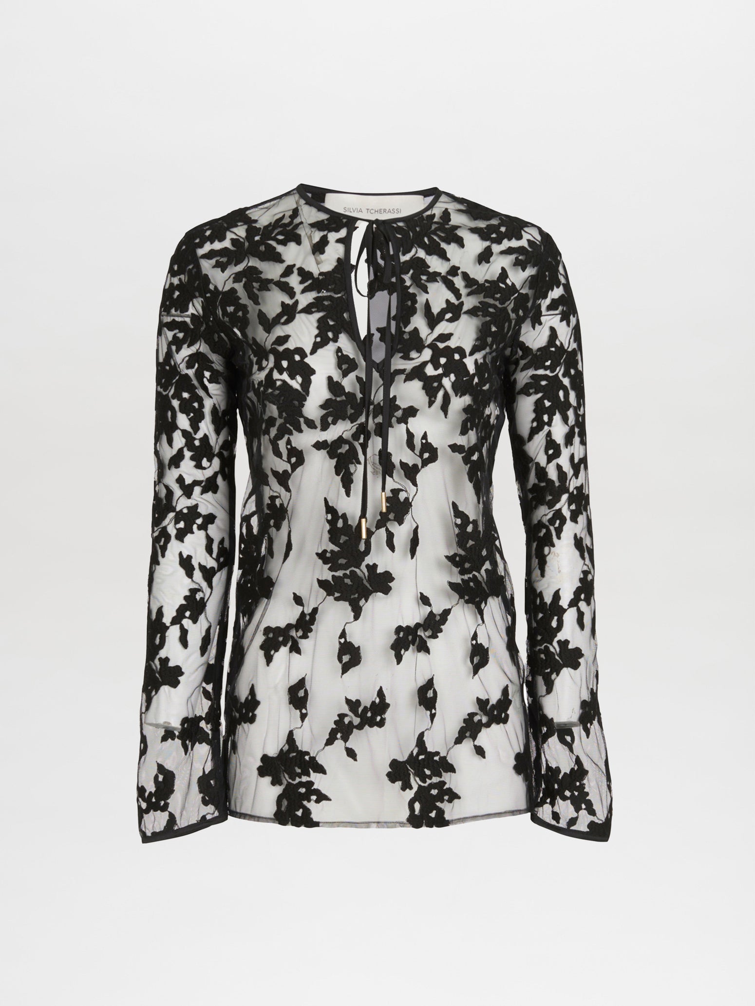 A sheer black and white floral lace blouse with long sleeves and a tie at the neckline elegantly mirrors the Tosca Blouse Black Velvet by Silvia Tcherassi, presented on a plain white background.