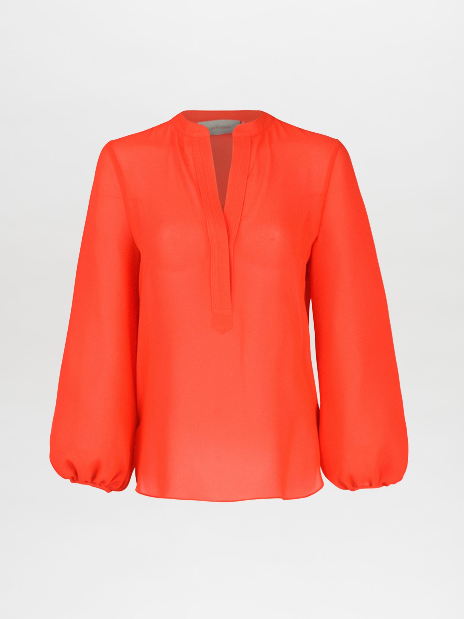 The Silvia Tcherassi Triora Blouse in tangerine is showcased on a white backdrop. It features a V-neck, relaxed fit, and elastic cuffs for puffed sleeves—ideal for a chic outing.