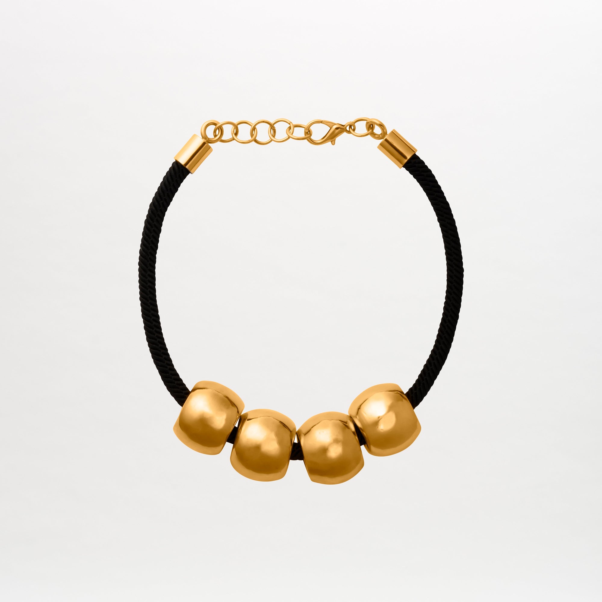 The Tristana Necklace by SVT DESIGNS showcases a black 3D cord adorned with four large smooth gold beads and gold-toned details on an adjustable chain with a lobster clasp closure. Made in Colombia, it's set against a plain white background.
