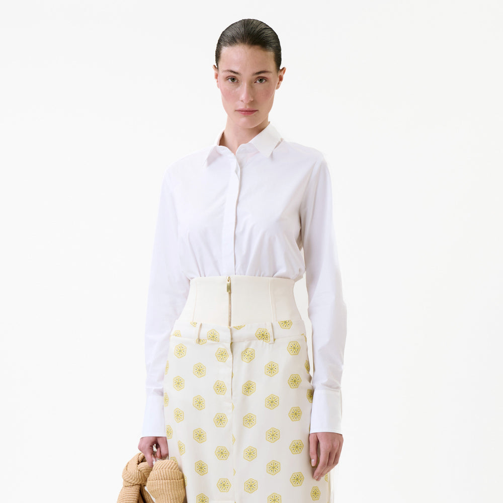 A model wearing a white long-sleeved Yemi Shirt tucked into high-waisted patterned trousers with a wide band and a front zipper.