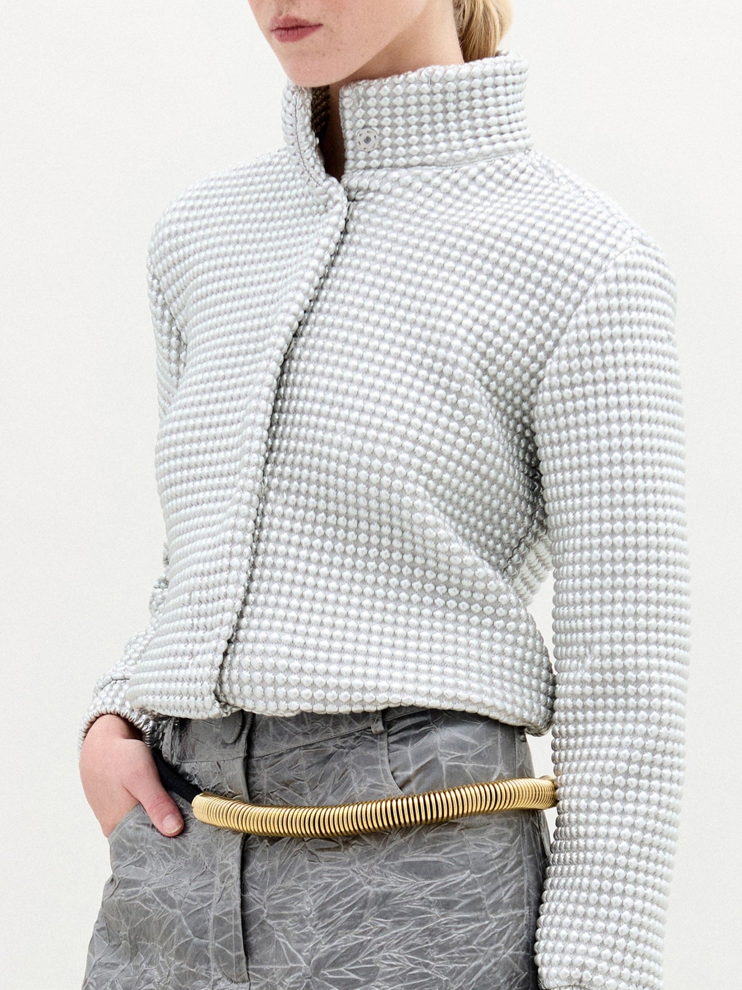 A person wearing the Zalta Jacket in color Silver with a golden belt on a white background.