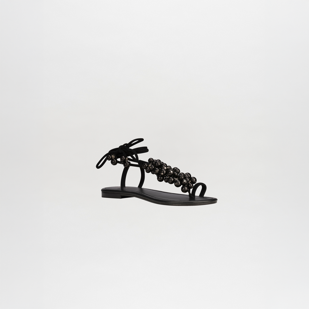 The Zaira Sandals are black leather sandals with wrap-around ankle straps and decorative beads, shown on a plain white background.