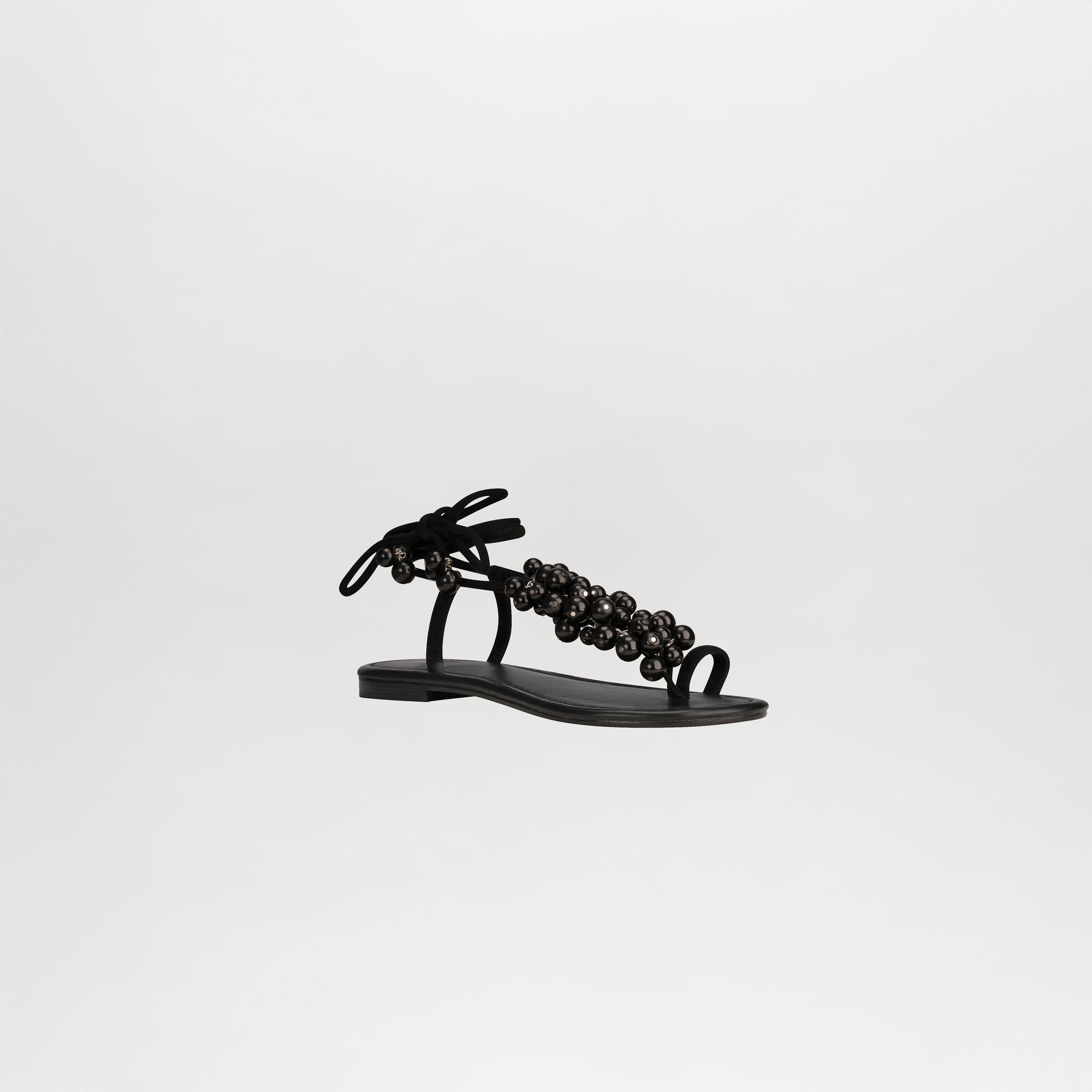 The Zaira Sandals are black leather sandals with wrap-around ankle straps and decorative beads, shown on a plain white background.