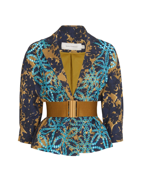 Juana Jacket Camo Navy with a geometric blue and gold pattern, featuring a wide tan belt and a double-breasted design. The cropped sleeves add a modern touch, while the interior lining is mustard yellow.