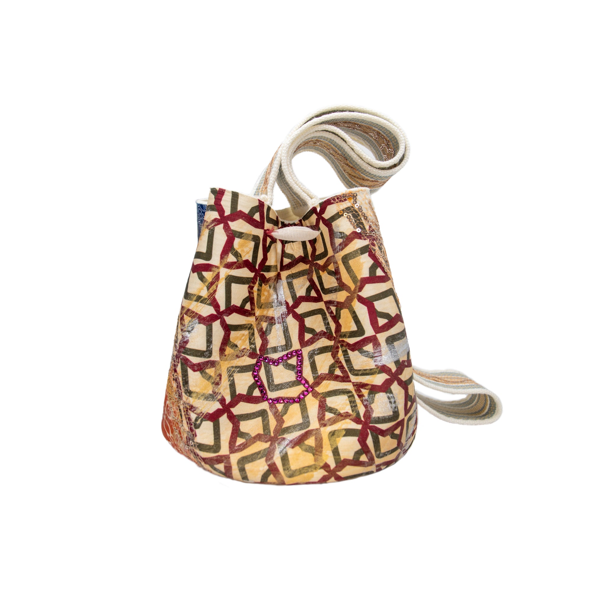 The Mochila Laaput Honey by SilviaTcherassiEU highlights Wayuu craftsmanship with a bucket shape, vibrant red, brown, and orange geometric patterns, an intricate drawstring closure, and a long hand-woven white strap.