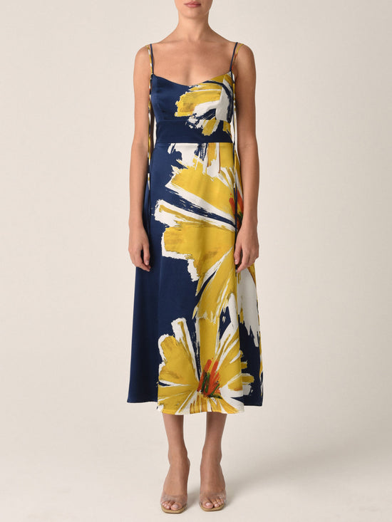 The Lizzo Dress Navy Floral Brushstrokes is a silk navy midi dress with spaghetti straps, showcasing a large yellow and white floral print alongside an A-line skirt.