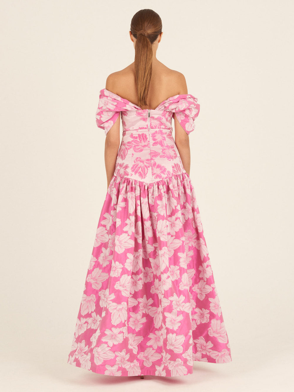 A woman with straight brown hair in a low ponytail is seen from behind wearing the Silvia Tcherassi Danu Skirt in Magenta Floral, featuring puffed sleeves and a full, floor-length silhouette.