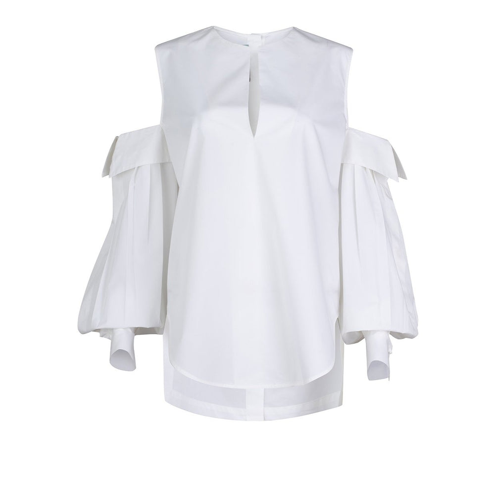 The Corato Shirt by SilviaTcherassiEU is a white cotton blouse with open shoulder design, featuring long pleated sleeves, a round neckline with a small V-shaped notch, loose fit, oversized cutouts, and a curved hem for effortless style.